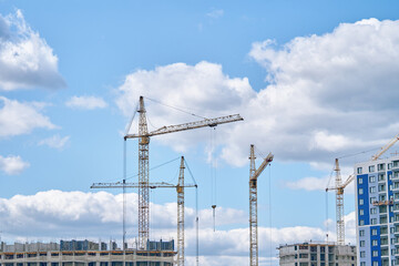 Industrial building cranes on background of cloudy sky. Construction site background. Hoisting cranes and multi-storey buildings of new city districts.