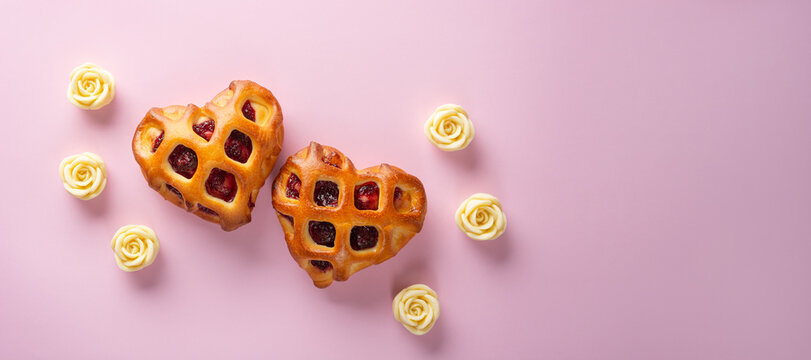 Valentines Day wide banner. Twain heart buns with berry jam and lattice crust on a light pink background with white chocolate roses. Flat lay, copy space for text, top view - Powered by Adobe