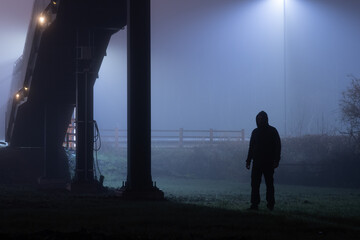A figure silhouetted under a bridge at night
