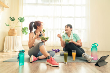 Two Asian women body size different in sport wear sitting healthy eating vegetable salad after...