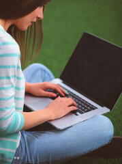 Naklejka premium Young woman with laptop sitting on green grass