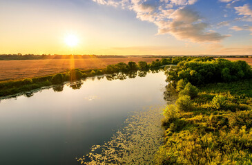 Naklejka premium Amazing view at scenic landscape on a beautiful river and colorful sunset with reflection on water surface and glow on a background, spring season landscape