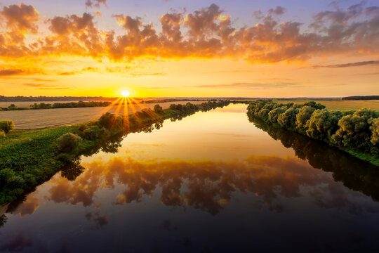 Amazing view at scenic landscape on a beautiful river and colorful sunset with reflection on water surface and glow on a background, spring season landscape © Yaroslav