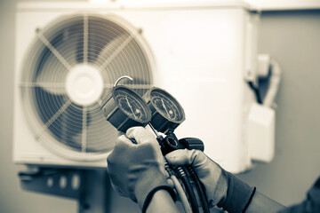 Mechanic air conditioner technician using manifold gauge checking refrigerant for filling home air conditioning and air duct cleaning and maintenance outdoor compressor unit.