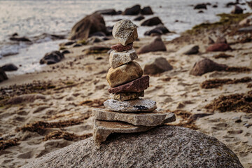 A cairn on a beach with water and sand in the blurry background
