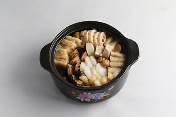 freshly hot stewed Peng cai with  seafood and meat in herbal sauce clay pot and yellow cover on white background Chinese traditional menu