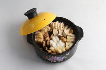 freshly hot stewed Peng cai with  seafood and meat in herbal sauce clay pot and yellow cover on white background Chinese traditional menu