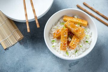 Bowl with fried chili tofu and white rice on a light-blue stone background, elevated view, horizontal shot