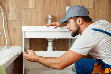 Concentrated plumber, male worker in uniform fixing sink and water pipe in the bathroom