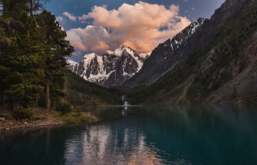 The shore of the lake and the setting sun illuminates the mountains covered with snow