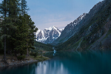 Fototapeta na wymiar Twilight over a mountain lake among the snow-covered rocks of the forest