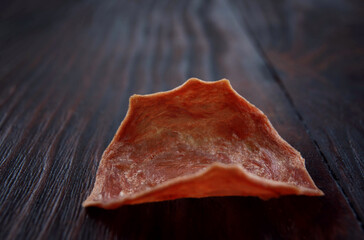 Meat chips. A single piece of dried meat lies on a dark wooden background.