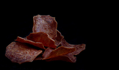 Meat chips on a black background. Beautiful placer of thin slices of dried meat.