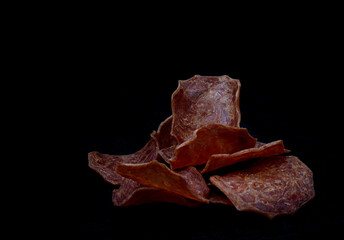 Meat chips on a black background. Beautiful placer of thin slices of dried meat.