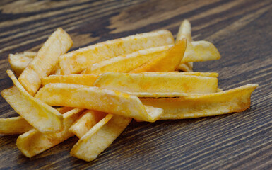 Potato chips in the form of sticks lie on a wooden board. Potato sticks are chips.
