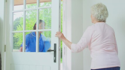 Senior woman at home using walking frame greeting female care worker in uniform at door - shot in slow motion
