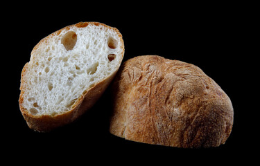 Ciabatta, a loaf of bread cut in half isolated on a black background.