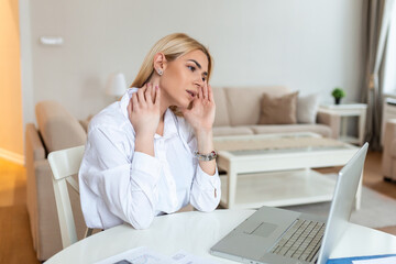 Young frustrated woman working at office desk in front of laptop suffering from chronic daily headaches, treatment online, appointing to a medical consultation, electromagnetic radiation, sick pay