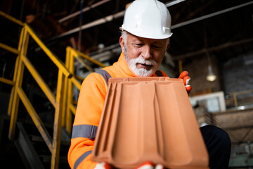 Industrial worker checking quality of roof tiles in manufacturing factory for building industry.