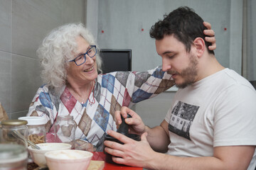 Senior mother holding her adult son face with love while he is cooking.