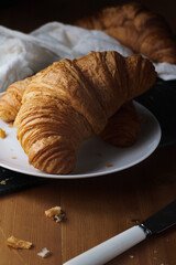Fresh croissants on a white plate set on a wooden breakfast table. Morning light from left side of shot. Copy space available