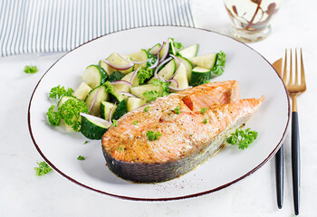 Baked salmon fish steak and fresh cucumber salad with red onions.