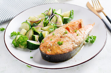 Baked salmon fish steak and fresh cucumber salad with red onions.