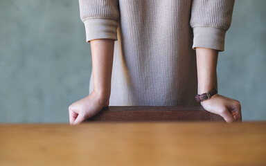 Closeup image of a woman standing and resting hands on wooden chair