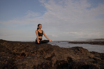 Morning meditation yoga on the beach. Asian woman sitting on the rock in Lotus pose. Padmasana. Hands in gyan mudra. Yoga retreat. Healthy concept. Copy space. Mengening beach, Bali