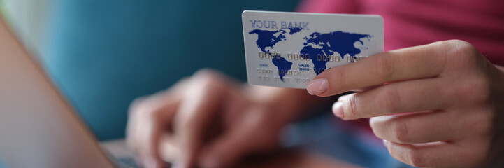 Woman holds bank card in hands and enters data into laptop closeup