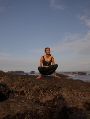 Fototapeta na wymiar Tolasana, Scale Pose. Seated lifted arm balance. Asian woman practicing yoga on the beach. Legs in Lotus pose. Strong arms. Healthy body. Yoga retreat in Bali. Copy space. Mengening beach