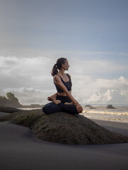 Fototapeta na wymiar Beach yoga. Asian woman practicing Parivrtta Sukhasana outdoor. Sitting in variation of Lotus pose. Easy twist pose. Stretching hips, knees, shoulders and spine. Mengening beach, Bali