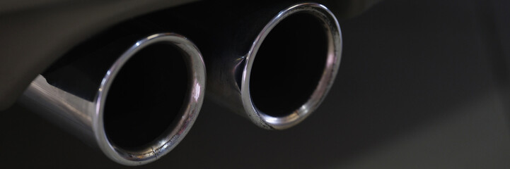 Twin chrome tailpipe of powerful sports car with black body and gray plastic parts