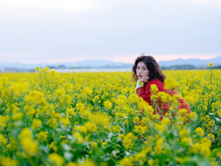 Naklejka na ściany i meble An Asian woman in a red trench coat stands in a field of rape flowers