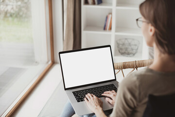 Young woman using laptop computer with white mockup screen at home. Freelance, student lifestyle, education, technology and online shopping concept. - obrazy, fototapety, plakaty