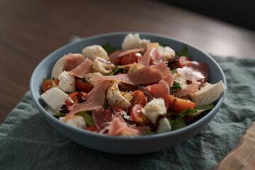 Fresh salad with prosciutto, mozzarella and cherry tomatoes in blue bowl