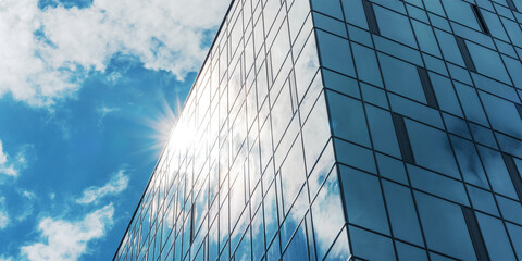 sunlight shines from behind office building with panoramic windows against blue sky with cumulus...