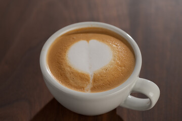 Flat white in white cup with simple latte art on walnut wood table