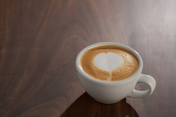 Flat white in white cup with simple latte art on walnut wood table