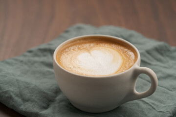 Flat white in white cup with simple latte art on walnut wood table with turquoise napkin