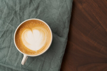 Flat white in white cup with simple latte art on walnut wood table with turquoise napkin