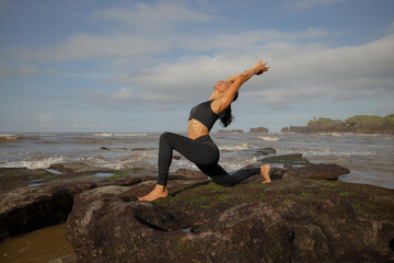 Morning beach yoga. Asian woman practicing Anjaneyasana. Low Lunge. Crescent Moon Pose. Equestrian Pose. Lunging back bending asana. Flexible healthy body. Yoga retreat. Mengening beach, Bali