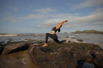 Morning beach yoga. Asian woman practicing Anjaneyasana. Low Lunge. Crescent Moon Pose. Equestrian Pose. Lunging back bending asana. Flexible healthy body. Yoga retreat. Mengening beach, Bali