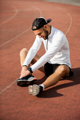 Unfortunate side of sports. Young handsome athlete sitting on the racetrack holding on to his injured knee