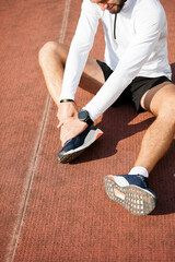 Unfortunate side of sports. Young handsome athlete sitting on the racetrack holding on to his injured knee