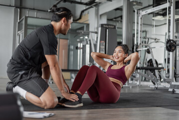 Fototapeta na wymiar Asian woman exercise with personal trainer in gym. Healthy woman doing abs workout in fitness with personal coach.
