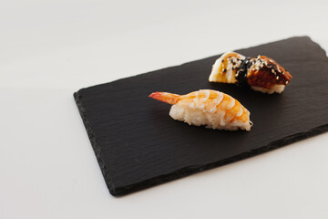 Nigiri and unagi Sushi japan food on black board plate with wooden chopsticks isolated on white. Sashimi sushi snacks and chopsticks japanese food with fish and seafood isolated on white close up.