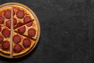 Pepperoni pizza Italian cooked cut into six pieces on wooden stand, top view dark background, with space to copy text.