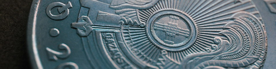Fragment of Kazakh 50 tenge coin with the country emblem and focus on shanyrak. Close-up. Blue tinted banner or headline for Kazakh economy or state. Macro
