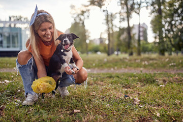 A young girl in the park is having a good time while cleaning up after her dog. Friendship, walk,...